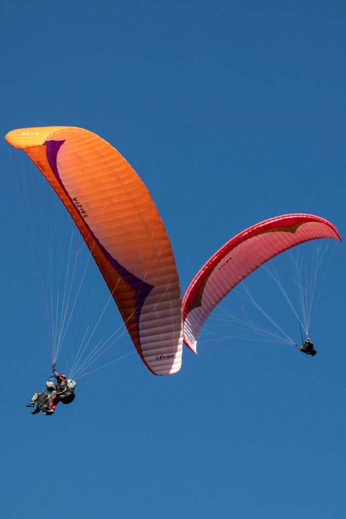 Two paragliders flying high above Danyang-gun under a clear blue sky.