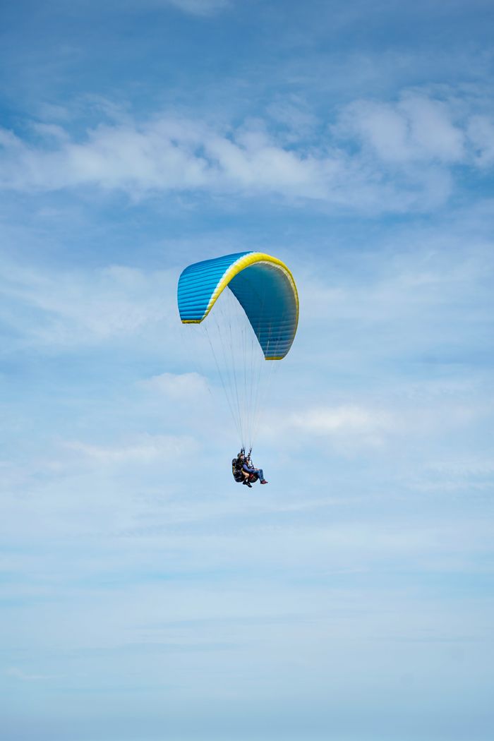 About A thrilling paragliding experience with two adventurers soaring under a blue parachute in clear skies.