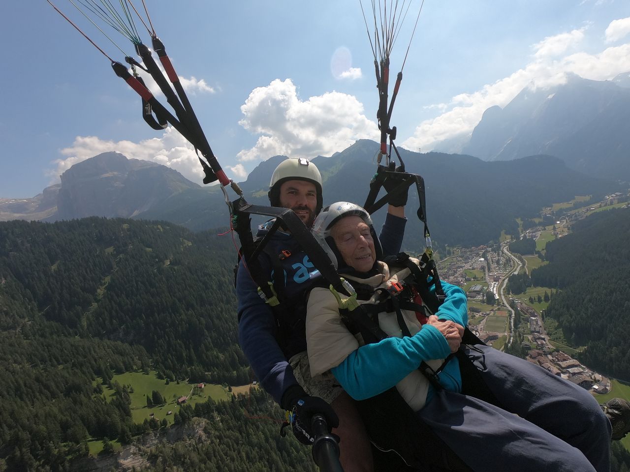 About Smiling elderly male in protective helmet near young trainer parachuting over mounts under cloudy sky