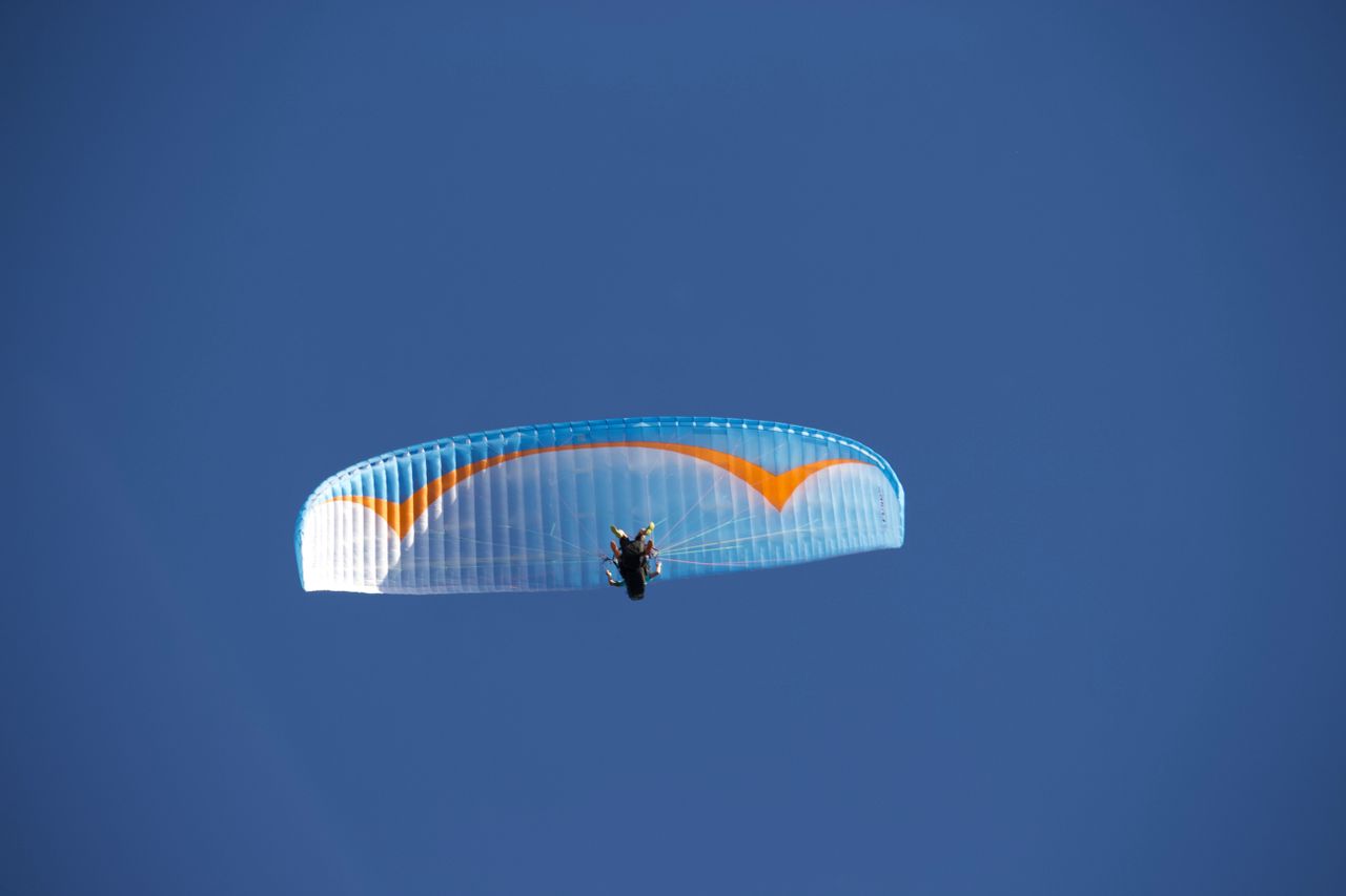 From below of anonymous paraglider with blue parachute flying against blue cloudless sky in nature in sunlight during practicing outside