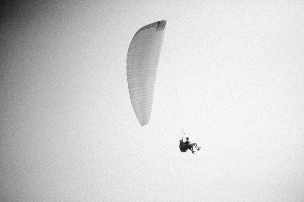 Black and white image of a paraglider soaring high in the sky, capturing the essence of flight and freedom.